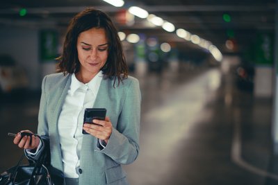  Media Alternativ Text  En kvinna använder sin mobiltelefon för att starta både parkering och laddning i samma app, APCOA FLOW – enkelt och stressfritt inne på parkeringsplatsen.
